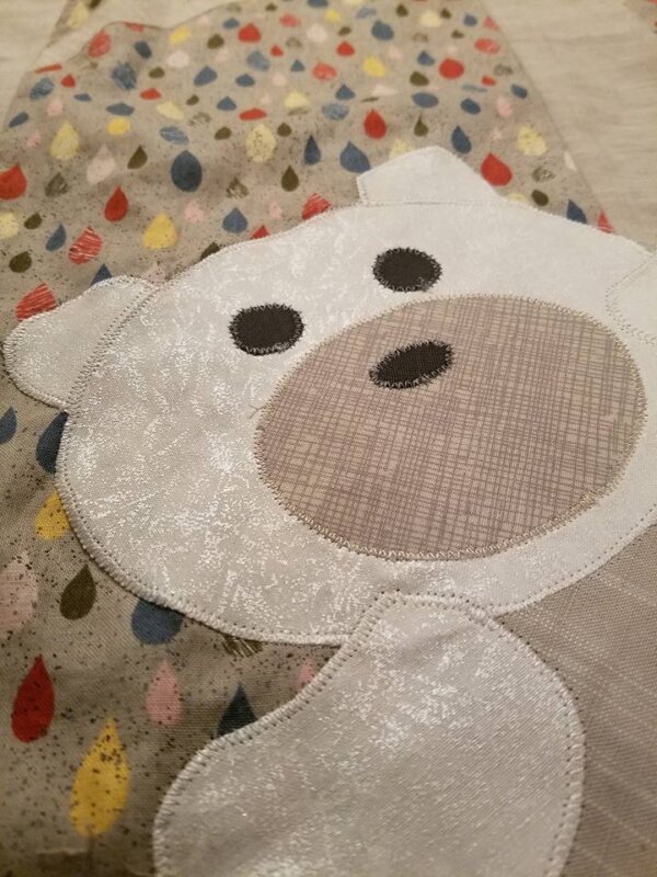 A white bear rests on a cozy baby quilt featuring a charming raindrop pattern, perfect for a woodland-themed nursery.